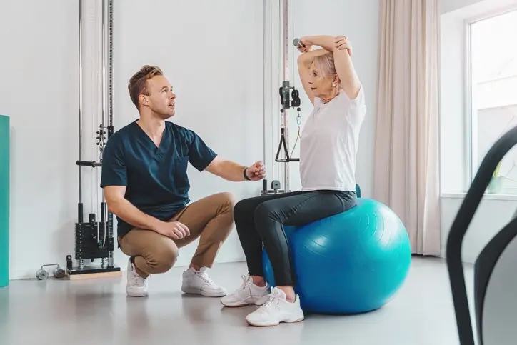 Nurse guides senior woman on Pilates ball through physical therapy in Shreveport, LA